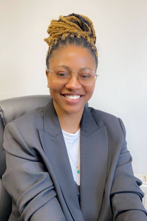 A smiling woman with braids and a grey suit jacket looks into the camera.