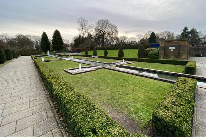A water fountain and green hedges surrounded by a path.