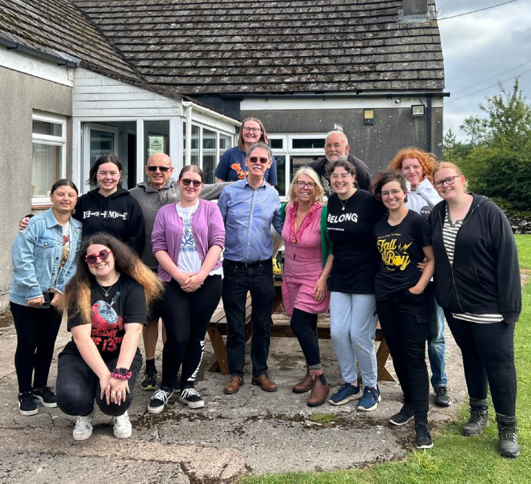 A group of happy people crowd together in front of a small, pebble-dashed building.