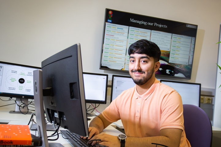 A Bradford student smiling and sat in a room with computers