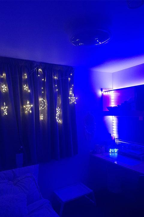 A room in blue lighting with fairy lights strung over the curtains.