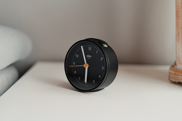 A black round alarm clock on a bedside table
