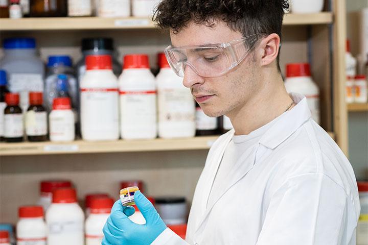A student in a lab coat in a lab setting, looking at a small pot.