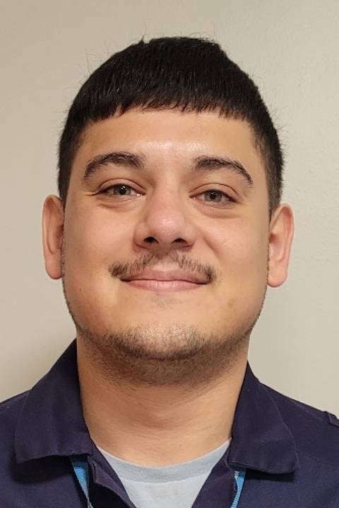 A young man smiles to the camera with a beige background.