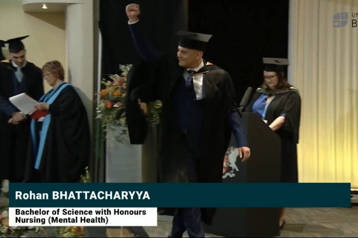 A still from a broadcast showing students in gowns and mortarboards at an awards ceremony.