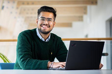 A student sitting behind a computer and smiling at the camera.