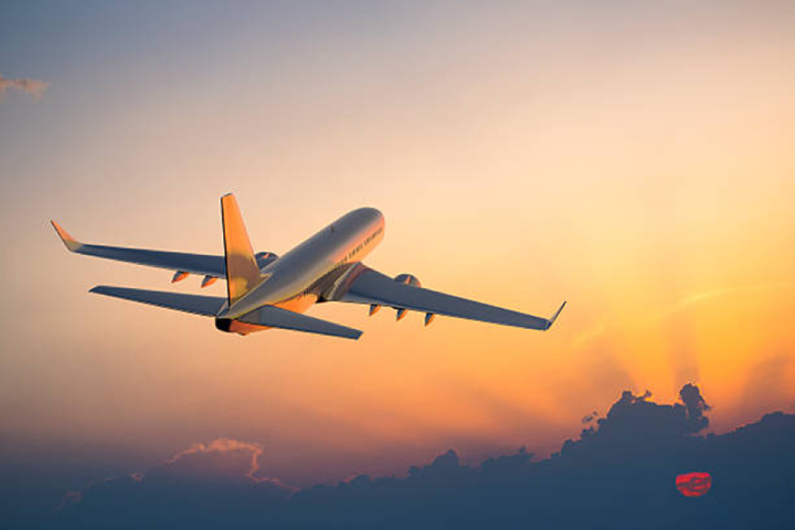 A white aeroplane appears against a golden sunset with silhouetted clouds.