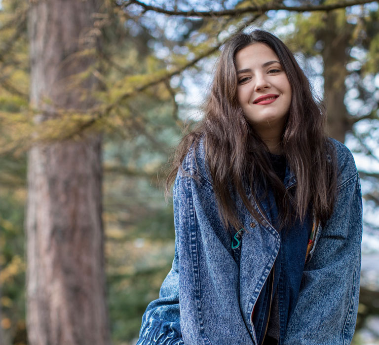 A student sitting in front of trees and smiling at the camera