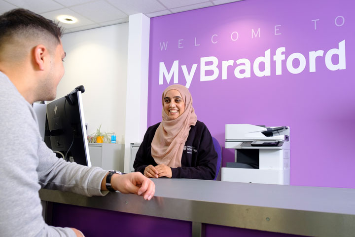 A student sitting with an employee at the counter with MyBradford sign in the background