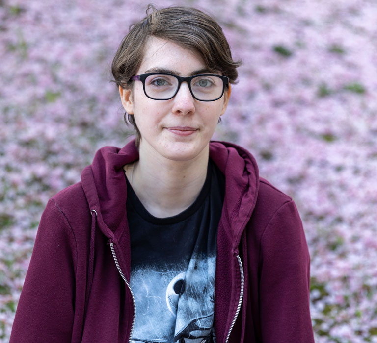 A student sitting in front of a hill covered in cherry blossoms looking at the camera