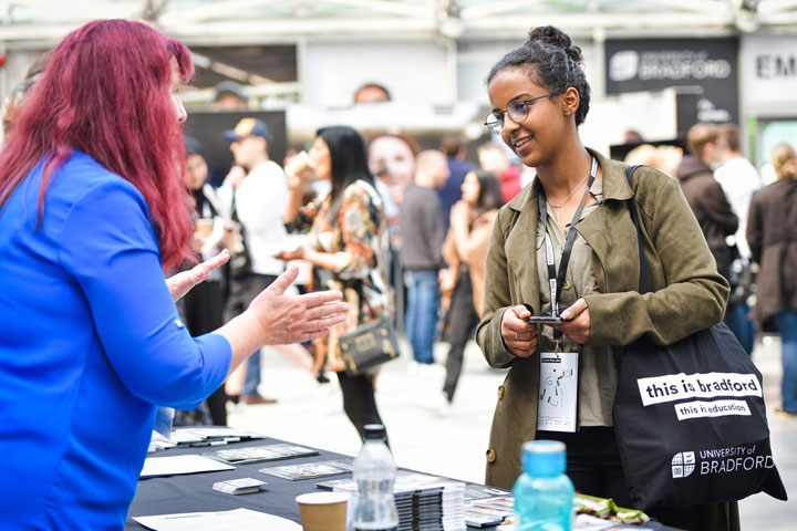 A prospective student at an Open Day speaking to a staff member while other attendees are in the background