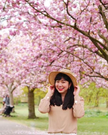 Giang wearing a hat in front of a tree bursting with beautiful pink blossoms.