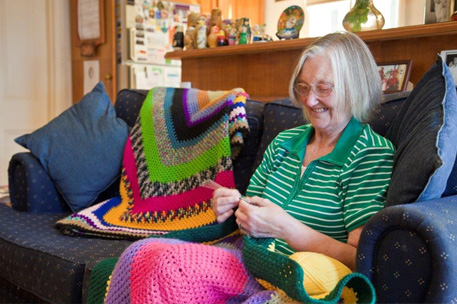 An elderly person sat knitting on a sofa.Copyright Cathy greenblat photography.
