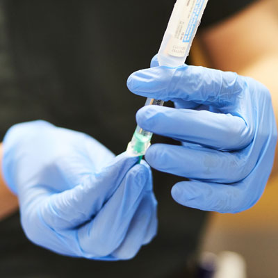 Two hands wearing medical gloves, holding a syringe.