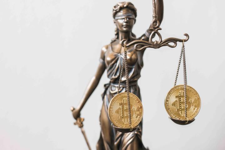 Statue of Lady Justice holding scales. Coins representing the bitcoin cryptocurrency are at the end of each arm of the scales