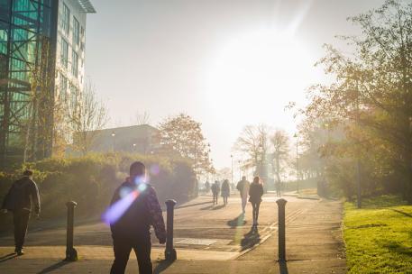 Several students walking up the hill towards Richmond Building, with a bright sun in the sky.