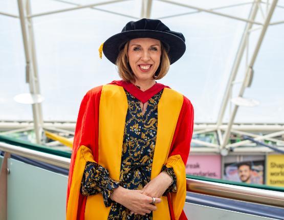 A woman standing smiling in graduation robes