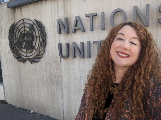 A University academic smiles and stands in front of sign for the United Nations