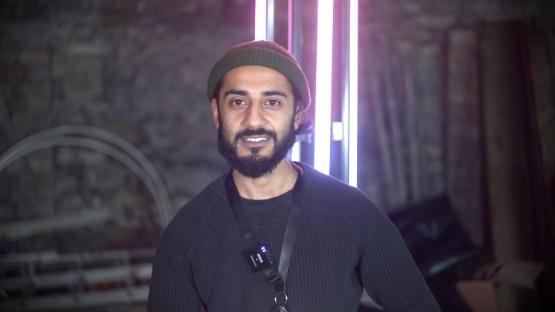 A person smiling wearing a beanie hat in front of a neon lighting strip