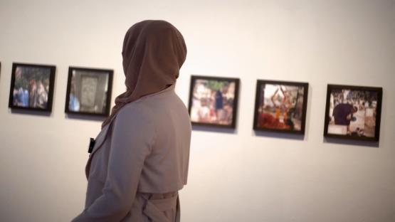 A person with their back to the camera looks over at a series of photographs hanging on a wall at an exhibition