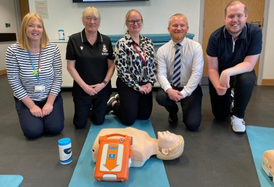 Five people crouched down on their knees behind a CPR dummy