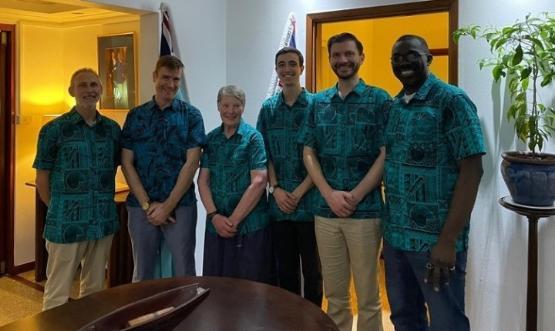 five people wearing the same Hawaiian style shirt stand next to each other
