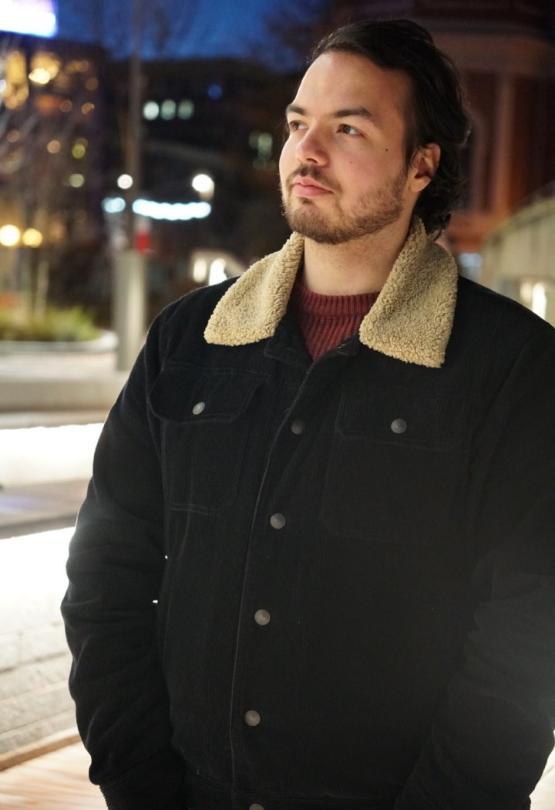 former student wearing a jacket looks into the distance in a street