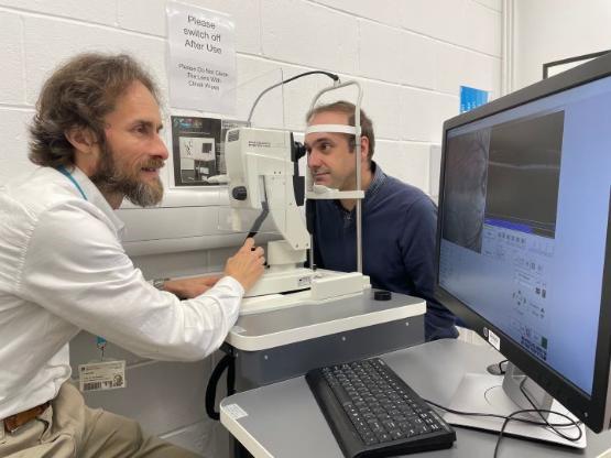 a person sits down and leans forward for a mock eye test opposite another person