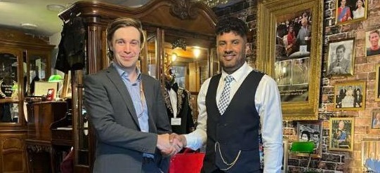 Two smartly dressed men shake hands in a tailor shop