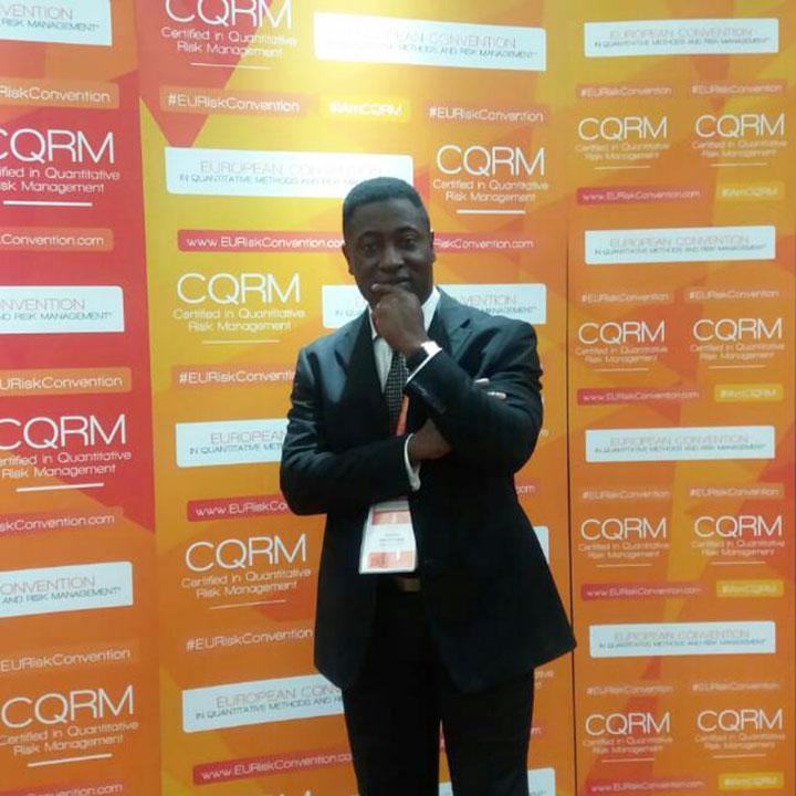 A photo of Dr Rexford Attah-Boakye in front of some display boards at the Africa Quantitative Risk Conference