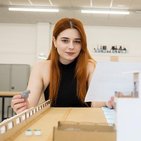 Student smiling at the camera behind a model structure.