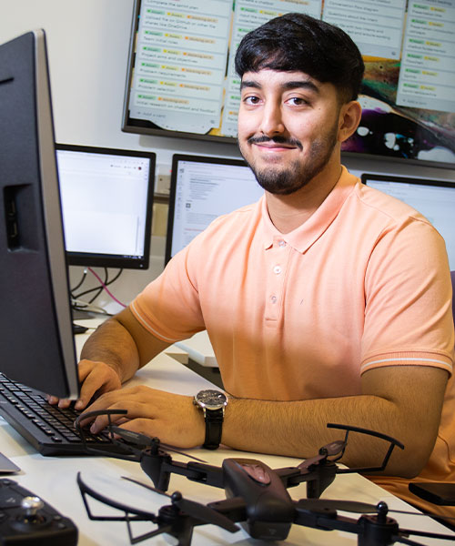 A student on a computer, smiling at the camera.
