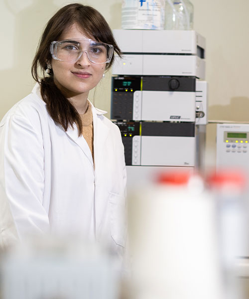 A student in a lab, smiling at the camera.