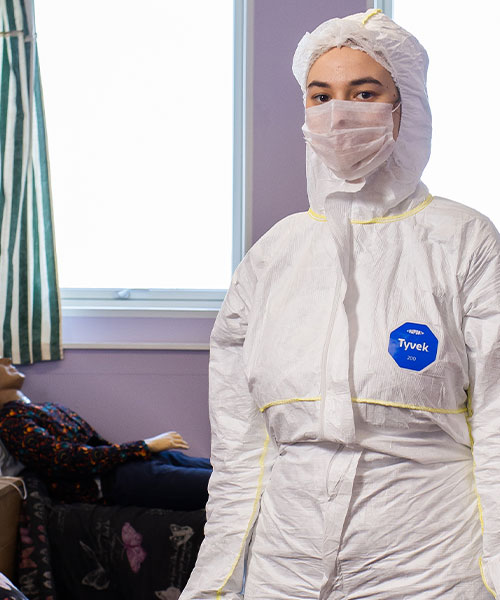 A student in PPE at a simulated crime scene, looking at the camera.
