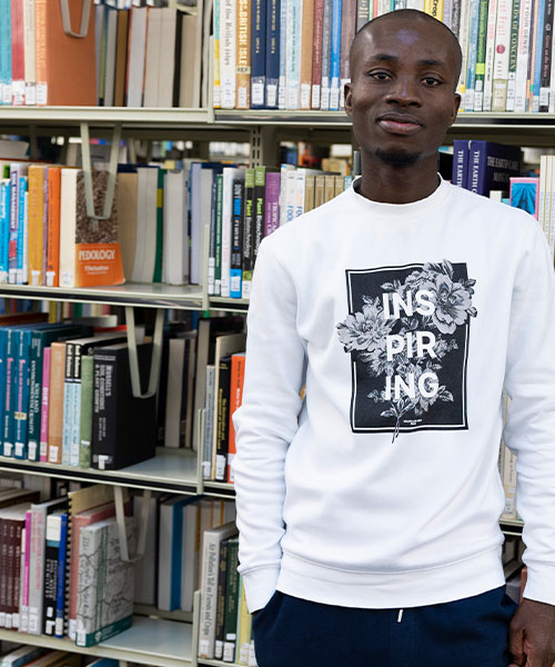 A student in a library, smiling at the camera.